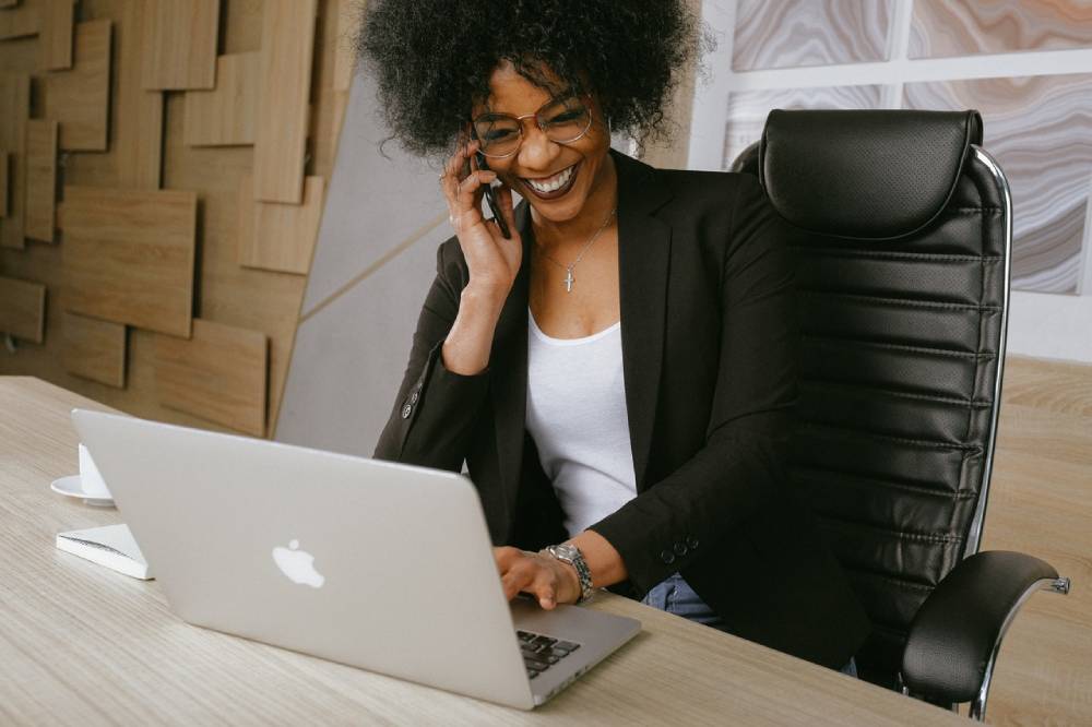 A woman in a business attire holding a mobile phone and a laptop